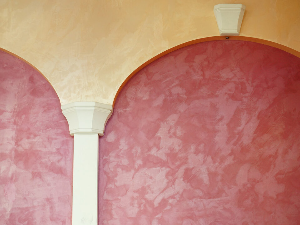 A closeup of a pink wall with an arched design